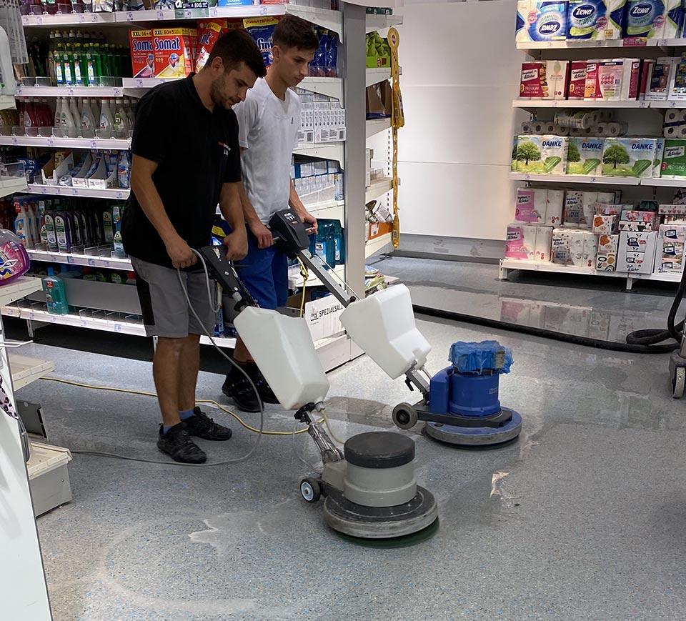 Zwei Männer reinigen den Boden eines Geschäfts mit professionellen Reinigungsmaschinen.