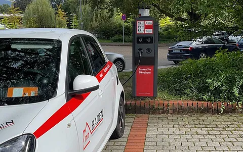Ein Elektroauto mit einem roten und weißen Design parkt an einer Ladestation. Die Station zeigt Ladeanschlüsse und Anweisungen zum Aufladen.