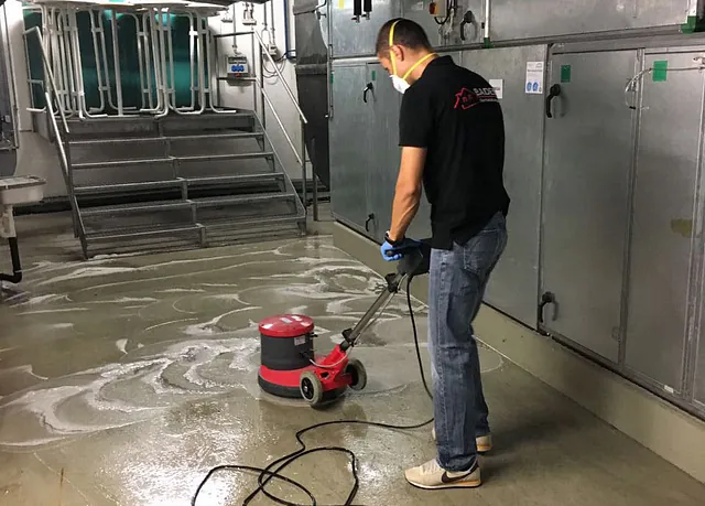 Mann mit Schutzmaske und Handschuhen reinigt den Boden mit einer elektrischen Reinigungsmaschine in einem gewerblichen Raum.