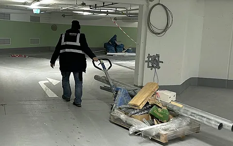 Arbeiter in Warnweste schiebt einen Handwagen mit Baumaterialien in einer Parkgarage.