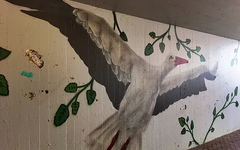 Wandmalerei eines fliegenden Vogels mit ausgebreiteten Flügeln, umgeben von grünen Blättern.