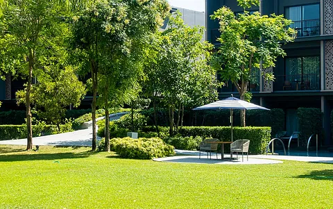 Grüne Gartenlandschaft mit Rasen, Bäumen und einer Sitzecke unter einem Sonnenschirm.