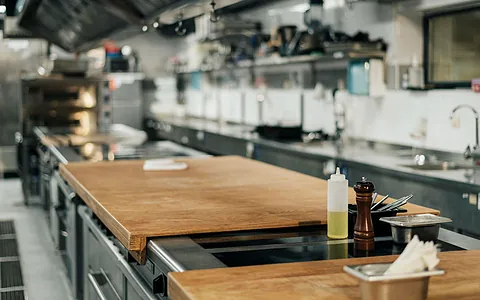 Moderne Restaurantküche mit Holzarbeitsfläche, Kochutensilien und Geräten im Hintergrund.