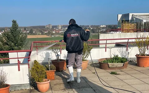 Mann in schwarzer Jacke reinigt Terrasse mit Hochdruckreiniger.